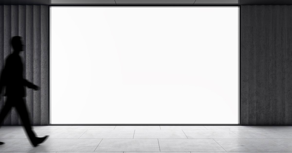 A large, white, wall-sized screen is attached to a wall alongside paneling and white tile flooring. A man is walking by it.