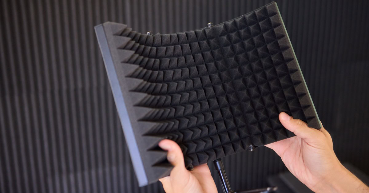 A close-up of a person holding a black foam acoustic panel used to soundproof a room with both hands.