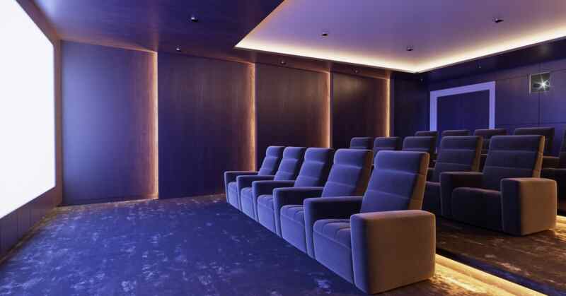 Modern home theater with rows of plush blue recliner seats facing a large screen in a dimly lit room.