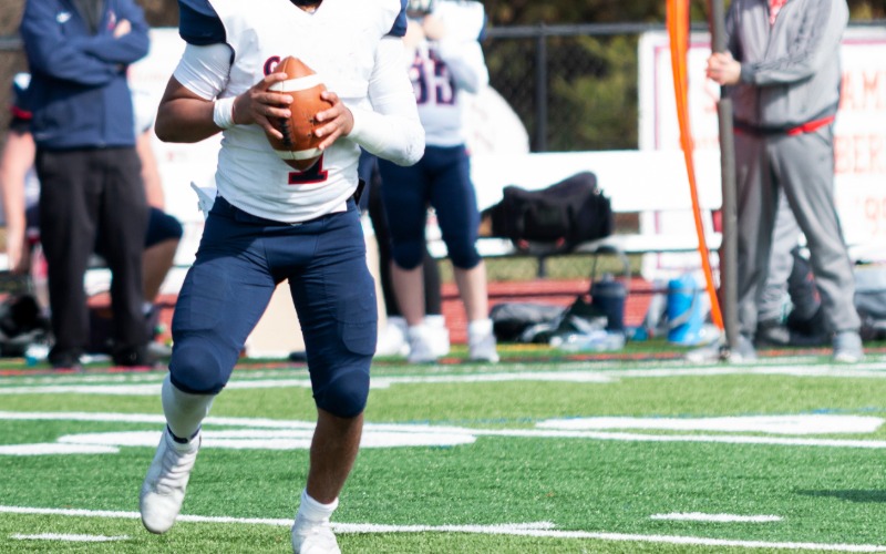 A football player holding a ball while preparing to throw during a game on a field with other players nearby.