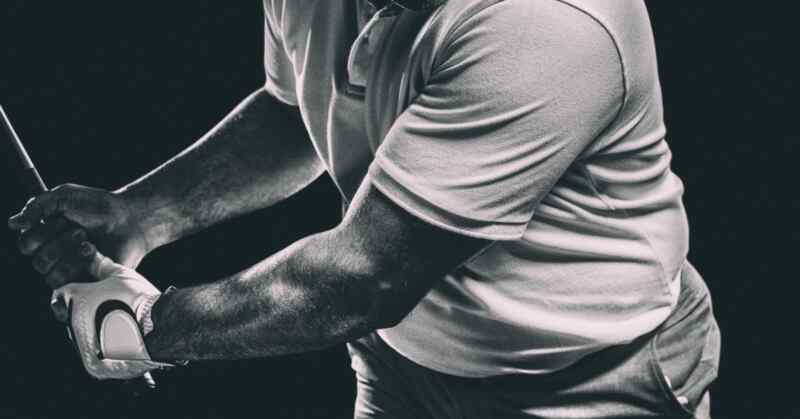 A cropped black-and-white view of a person gripping a golf club while swinging against a dark background.